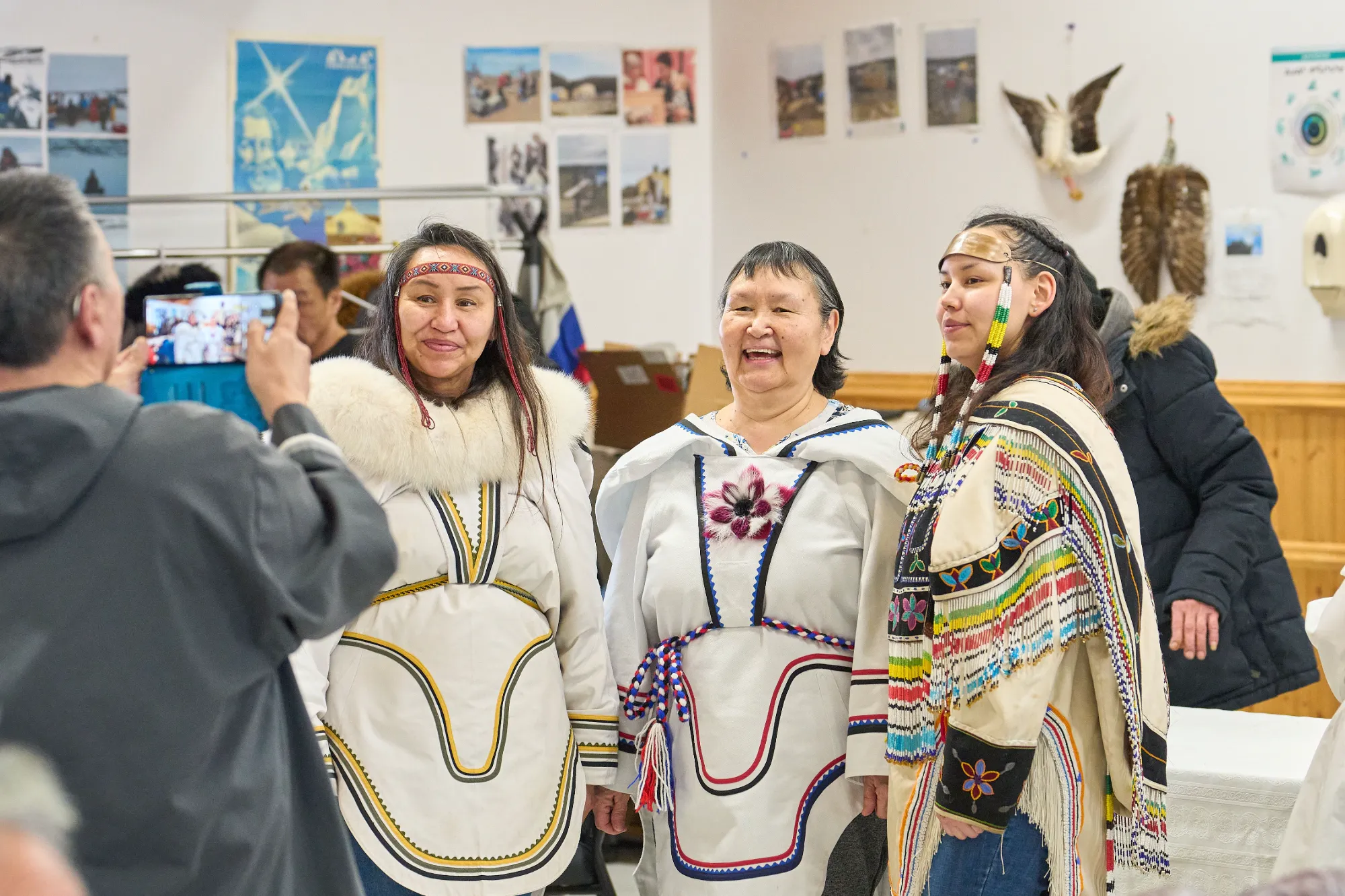 Three members of the community pose together for a photograph. They are wearing traditional Inuit garb.