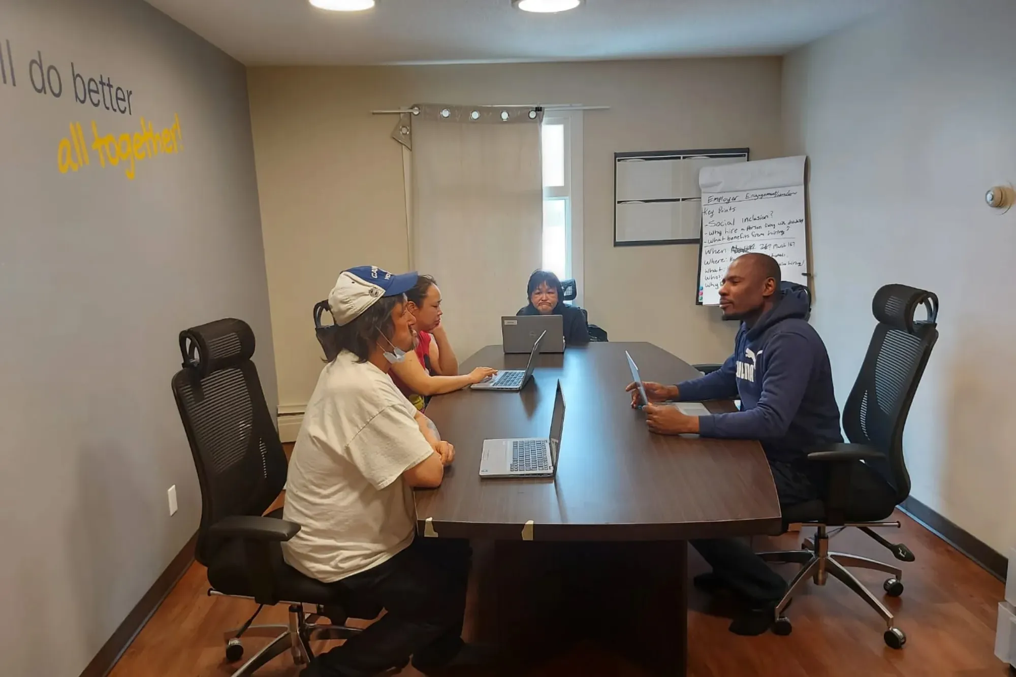 A man sits across a table from several community members, all with laptops in front of them.