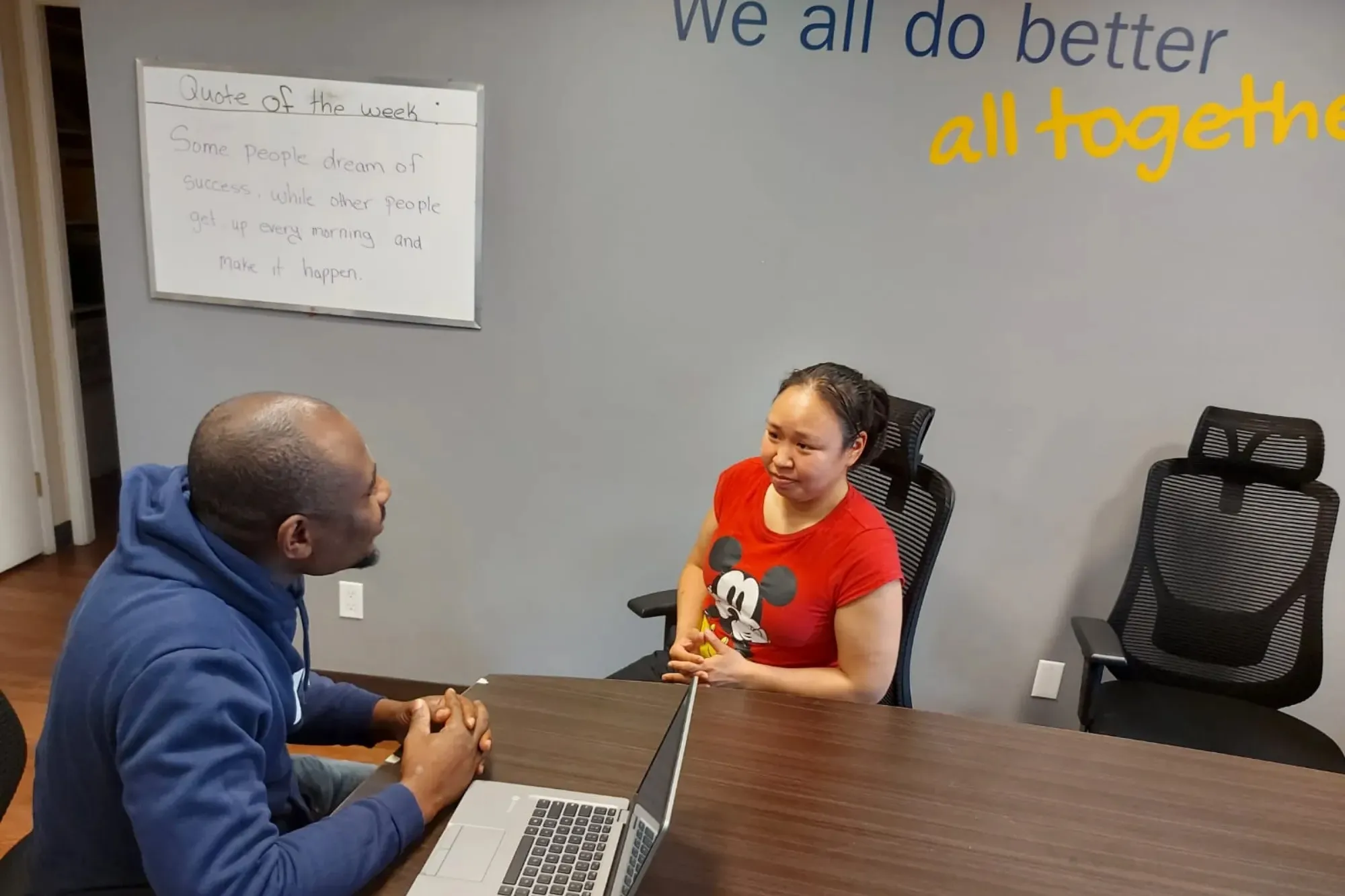 A man sits across a desk from a woman, engaged in conversation with her.